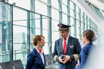 Portrait of Mature pilot talking to flight attendants in airport with yellow lens flare