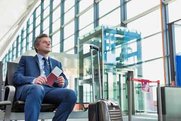 Portrait of Mature businessman sitting and holding his passport while waiting in gate for boarding...