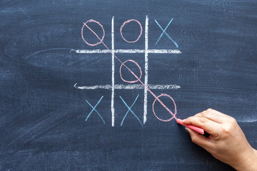 hand drawing a game of tic tac toe with colored crayons on a black chalkboard