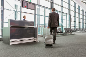 Rear view of mature businessman walking with his suitcase on his gate for boarding in airport