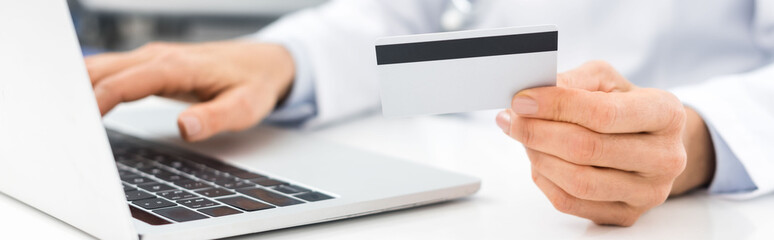 panoramic shot of doctor using laptop and credit card in clinic