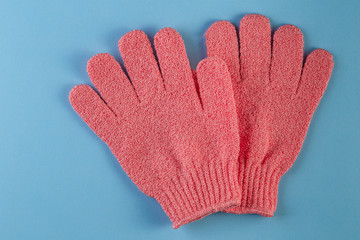 A pair of pink massage gloves for shower on blue background. Gloves for use in the shower for massage and scrub. Beauty background with cosmetic products. Beauty, health and spa concept