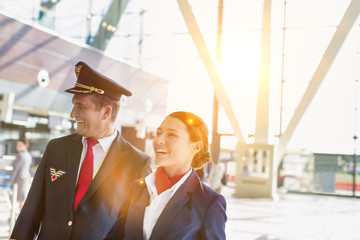 Portrait of mature pilot and attractive flight attendant walking while smiling in airport © MDBPIXS