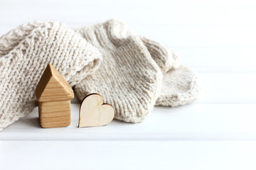 house and a heart made of wood on a background of a scarf and mittens. cute warm house