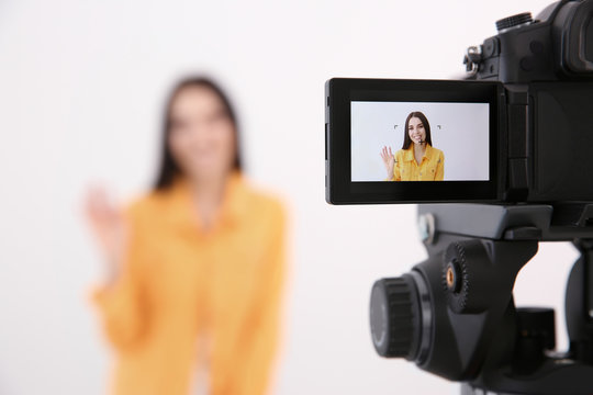 Young blogger recording video against white background, focus on camera screen