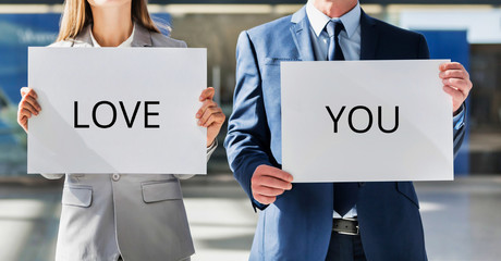 Business couple holding white placard with I love you sign