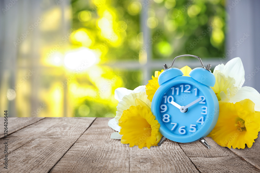 Poster alarm clock and flowers on table against blurred background, space for text. spring time