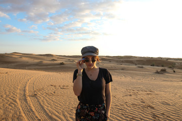 Young woman with hat touching her sunglasses in the Sahara desert