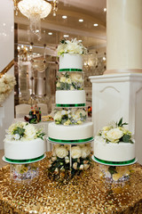 A large royal cake in white color decorated with many flowers and roses at a luxury wedding with a very beautiful decor. Dessert for festive dinner of the bride and groom.