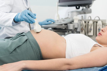 cropped view of doctor examining belly of pregnant woman with ultrasound scan in clinic