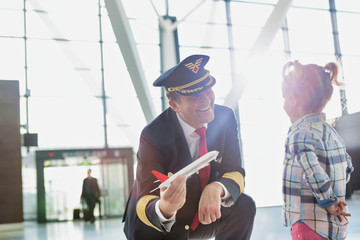 Portrait of mature pilot holding airplane toy while playing with cute little girl in airport