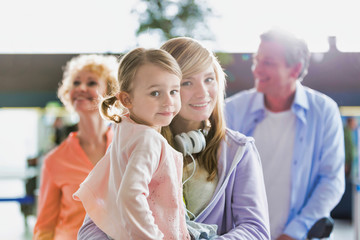 Portrait of young teenage girl carrying her cute little sister while queueing with their parents for check in at airport