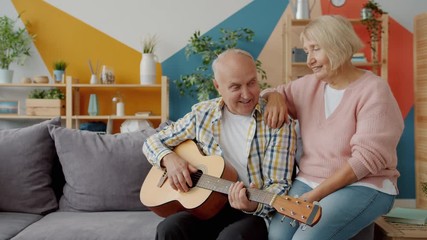Retired couple man and woman are playing the guitar and singing enjoying romantic day indoors at home. Family life, retirement and lifestyle concept. - Powered by Adobe