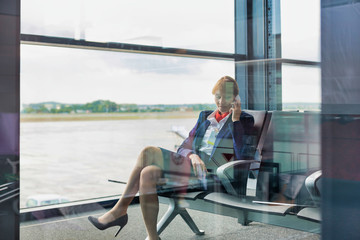 Fototapeta premium Photo of young attractive airport staff sitting while talking on smartphone
