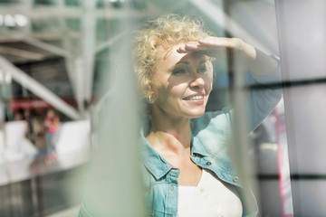 Portrait of mature woman covering her eyes from sunlight while looking through the window in airport