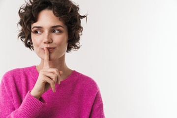 Image of pleased curly woman making silence gesture and looking aside