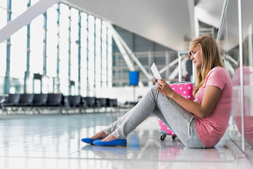 Portrait of young teenage girl sitting on the floor and using digital tablet while waiting for her flight in airport