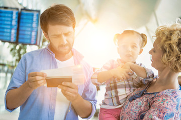 Man looking on boarding pass while his wife is carrying their daughter in airport