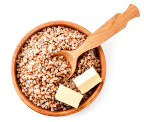 Boiled buckwheat in a wooden plate with a spoon and pieces of butter on a white. The view from the top