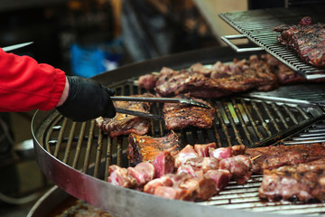 Male hand with tongs holding hot pork ribs. Fresh grilled meat. Street market. Food catering, party. Street festival. Barbeque.