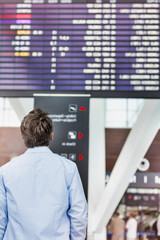 Rear view of mature man looking at his flght on screen in airport