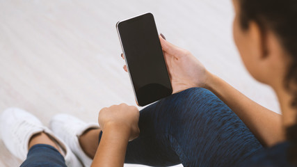 Young sporty woman holding mobile phone with blank screen indoors, closeup view. Mockup for design