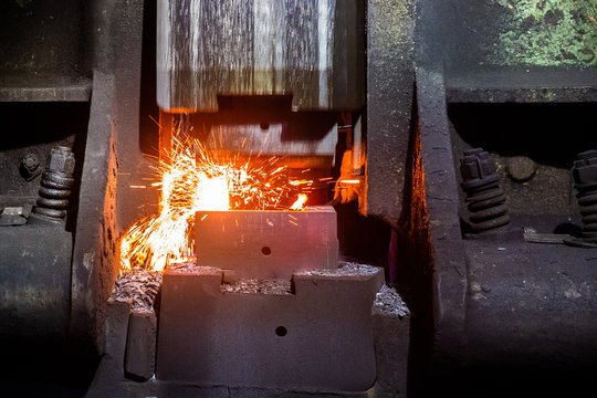 close-up frontal view of hot steel forging process with big mechanical hammer machine