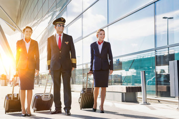 Mature pilot with young beautiful flight attendants walking in airport