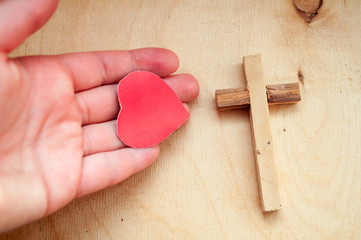 A hand holds a red heart and next to a wooden cross, a prayer for loved ones, healthcare, love, organ donation, family insurance and the concept of CSR, World Heart Day, World Health Day.