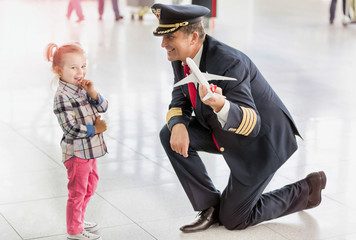 Portrait of mature pilot holding airplane toy while playing with cute little girl in airport