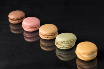 colored macarons on a black surface and with a reflection