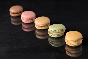 colored macarons on a black surface and with a reflection