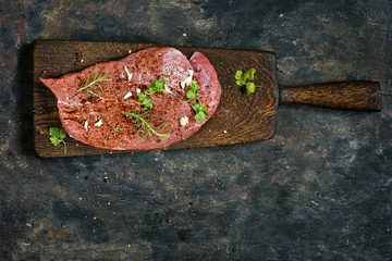 Fresh raw piece of beef steak with herbs and spices on wooden board on a dark background. A good piece of meat for cooking dinner.