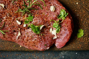 Fresh raw piece of beef steak with herbs and spices on wooden board on a dark background. A good...