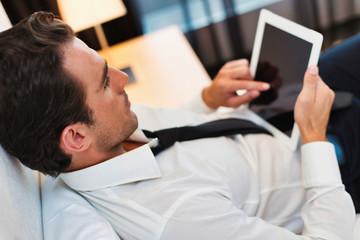 Mature businessman lying on bed while using digital tablet at home