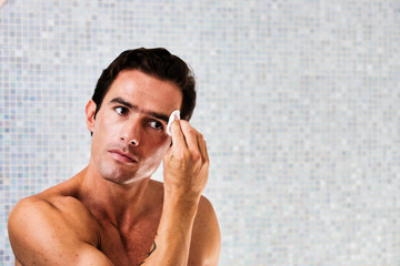 Portrait of young attractive man cleansing his face with cotton and toner in the bathroom