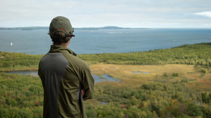 Adult man on a hike looking out over a vast forested landscape with valley, river and ocean