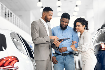 Spouses Buying Car Consulting With Dealer Guy In Dealership Store