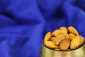 Almonds in a brass bowl on a blue background
