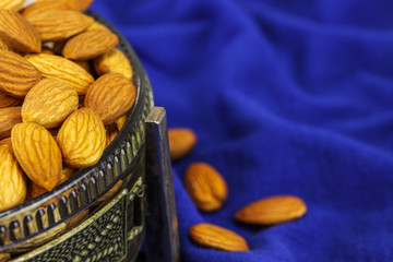 A glass bowl in a metal case filled with almonds on a blue background