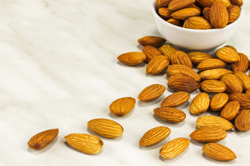 Almonds lie on a white marble surface and in a white bowl