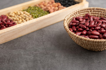 Red beans and grains in the wooden basket and in the wooden tray placed on the black cement floor. High angle view.