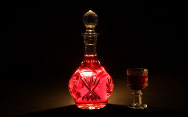 Backlit decanter with a red drink against a dark background.