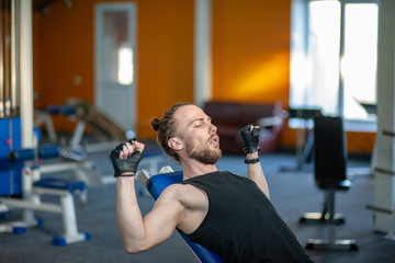 Fototapeta na wymiar Strong man lifting weight in sport club. Closeup guy training muscles with dumbbells in gym. Handsome fitness trainer doing power lifting exercises in fitness center.