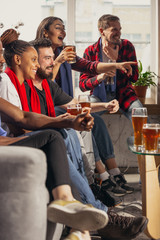 Excited group of people watching football, sport match at home. Multiethnic group of friend, fans cheering for favourite national basketball, tennis, soccer, hockey team. Concept of emotions, support.
