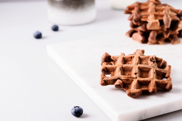 Homemade Chocolate waffles, milk and blueberries on white marble tray. Breakfast. Selective focus