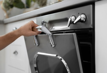 Man using modern oven in kitchen, closeup