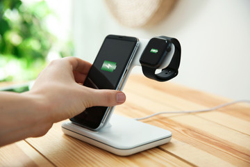 Man putting mobile phone onto wireless charger at wooden table, closeup. Modern workplace accessory