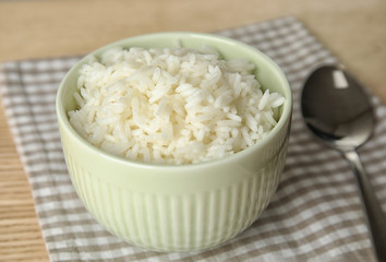 Bowl with tasty cooked rice on wooden table, closeup