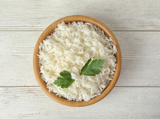 Bowl with tasty cooked rice and parsley on white wooden table, top view